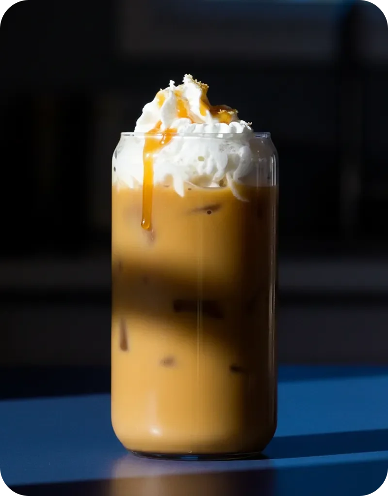 Iced coffee drink in a tall glass topped with whipped cream and caramel drizzle against a dark background.