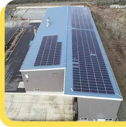 Aerial view of an industrial building with blue roof covered in solar panels, set on concrete foundation.