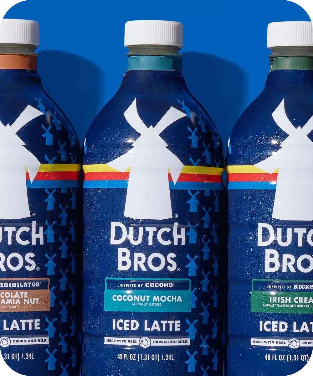 Three Dutch Bros bottled iced lattes in blue bottles with white windmill logos, featuring different flavored varieties.