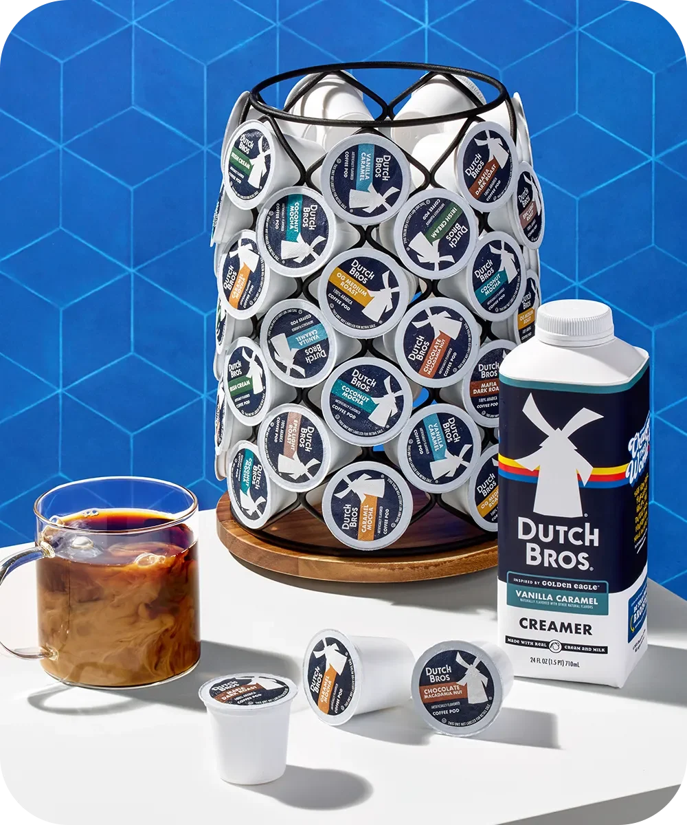 Dutch Bros coffee pod holder with creamer bottle, coffee cup, and coffee pods against blue geometric background.