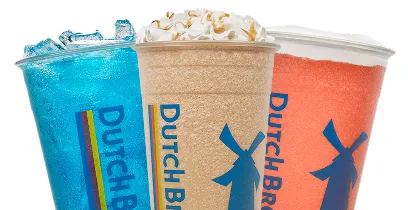 Three colorful Dutch Bros drinks - blue, tan, and orange beverages in branded cups with whipped cream topping.